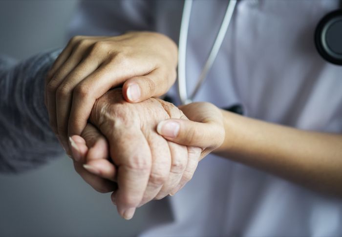 Mains d'une soignante en blouse serrant celles d'une patiente âgée