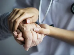 Mains d'une soignante en blouse serrant celles d'une patiente âgée